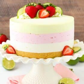 A key lime strawberry coconut ice cream cake on a white ruffled cake stand.