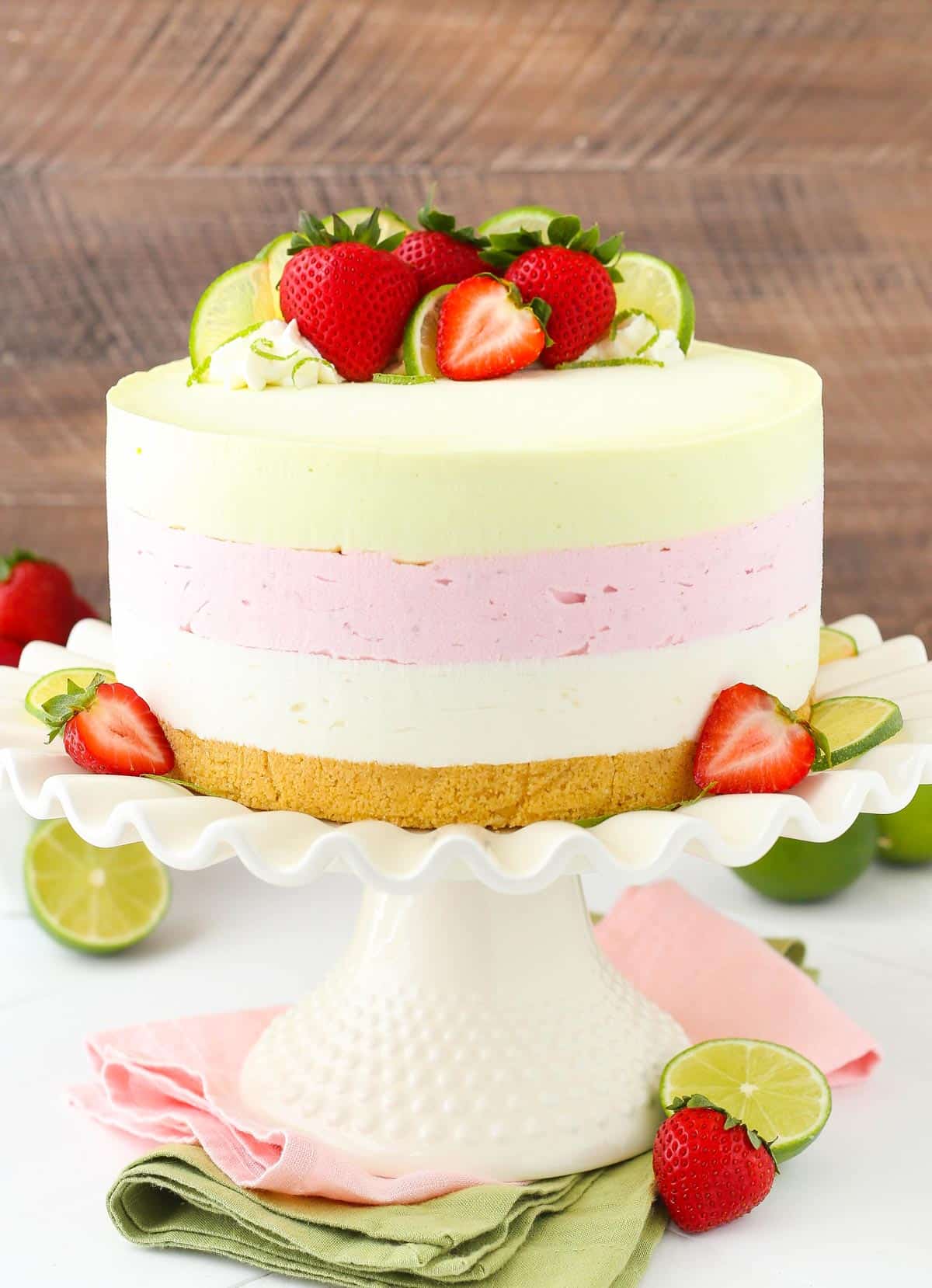 A key lime strawberry coconut ice cream cake on a white ruffled cake stand.
