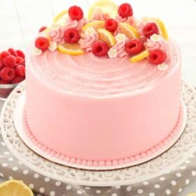 A lemon raspberry cake on a white cake stand.