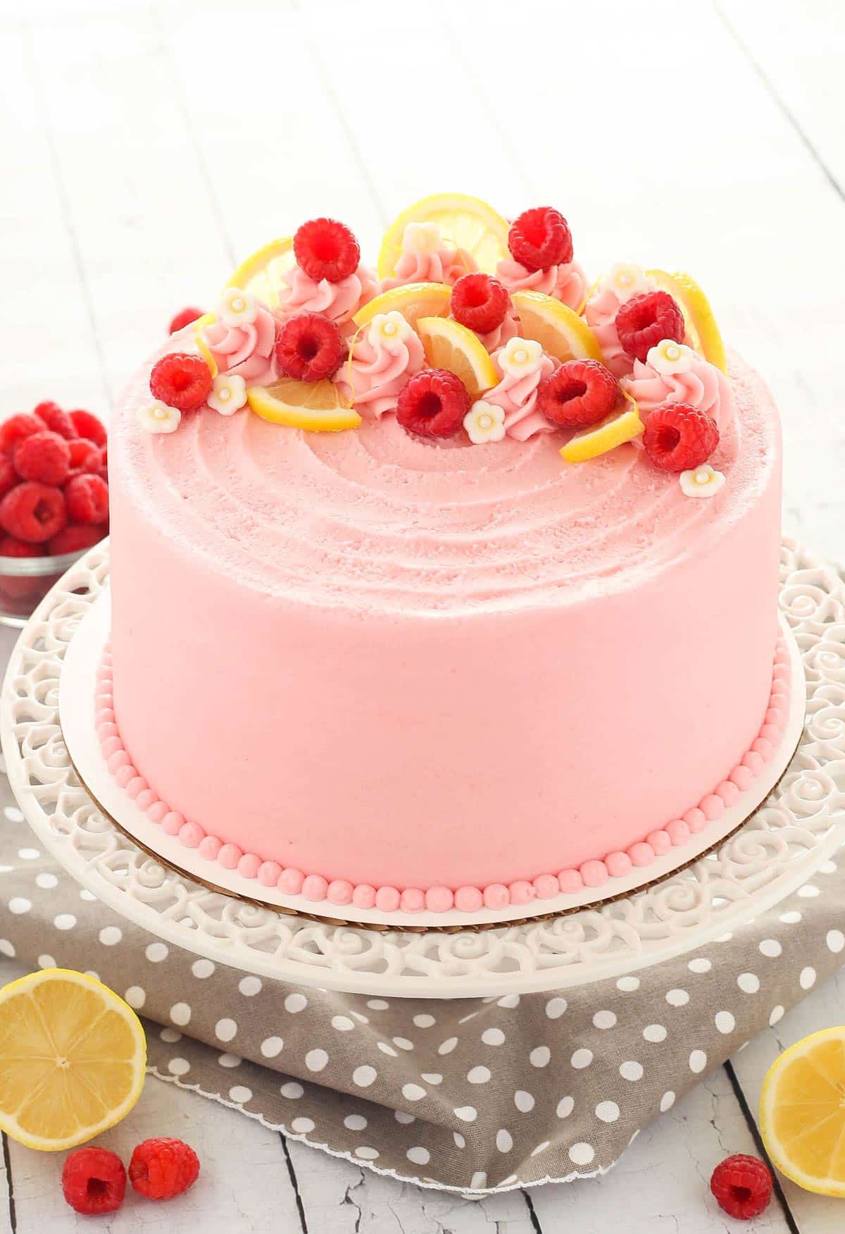 A lemon raspberry cake on a white cake stand.