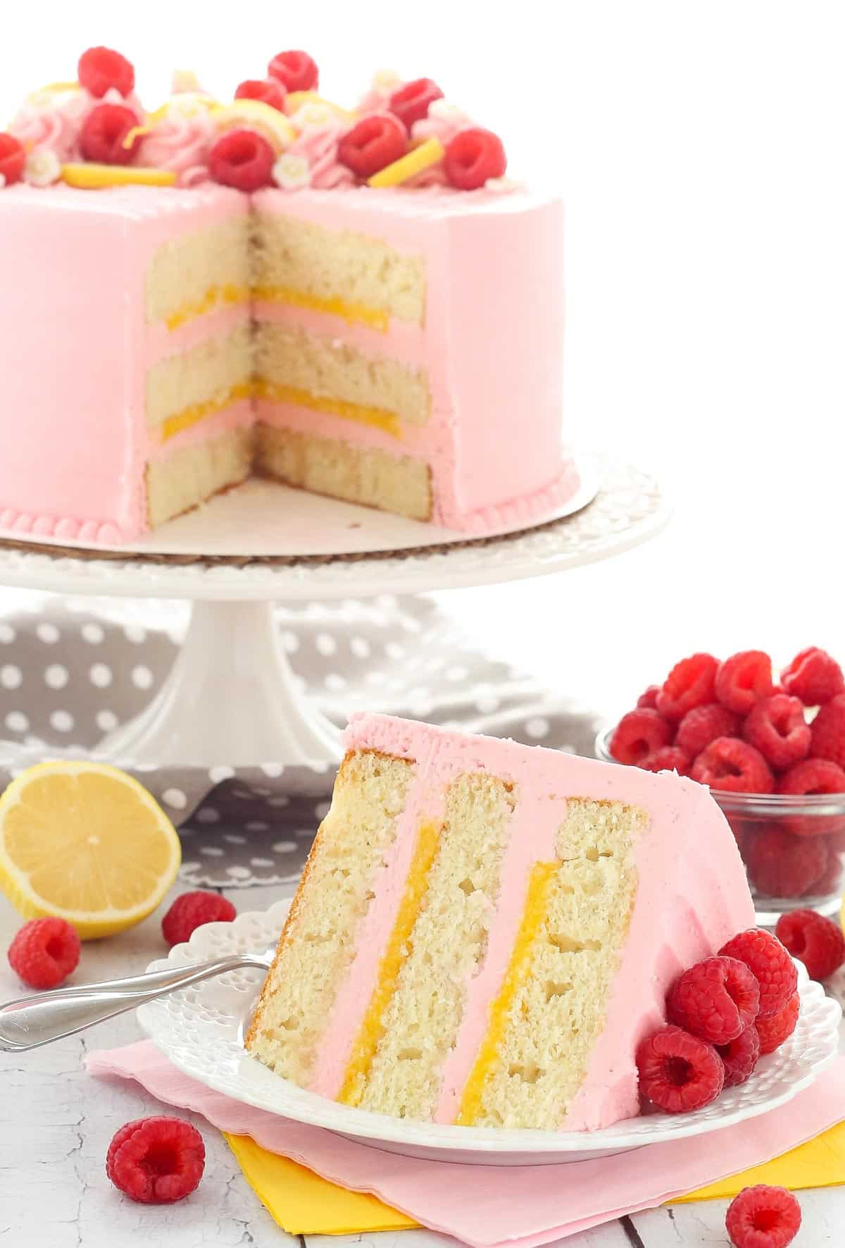 A slice of lemon raspberry cake with the rest of the cake in the background.