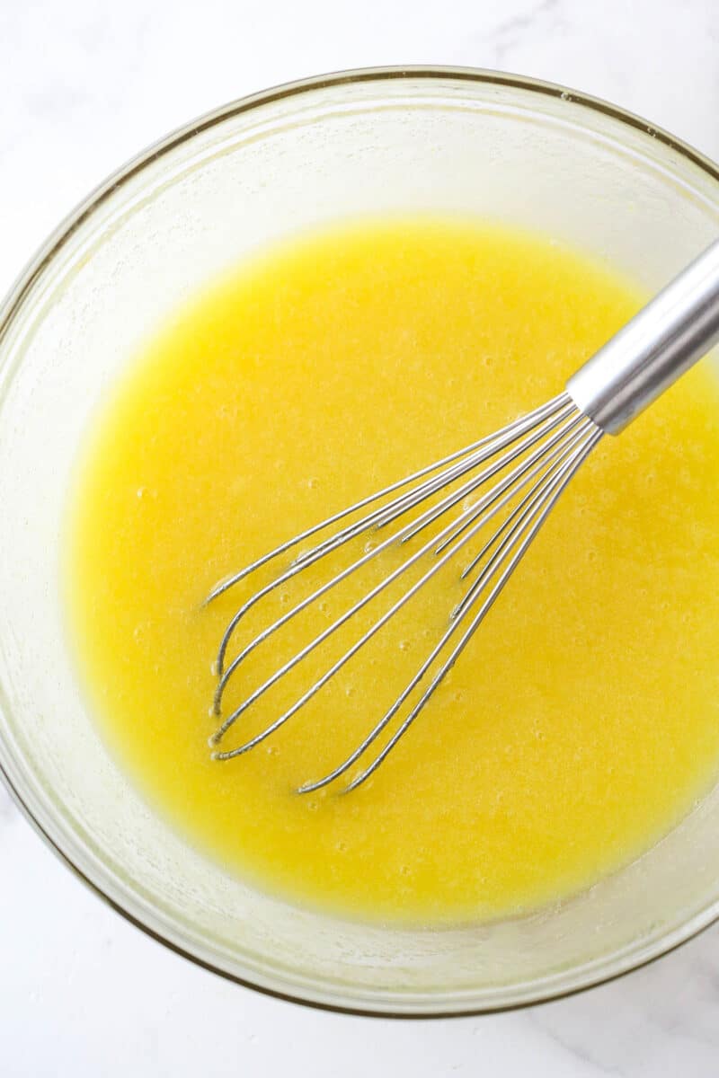 Whisking eggs into a mixture of oil, butter, sugar, and vanilla.