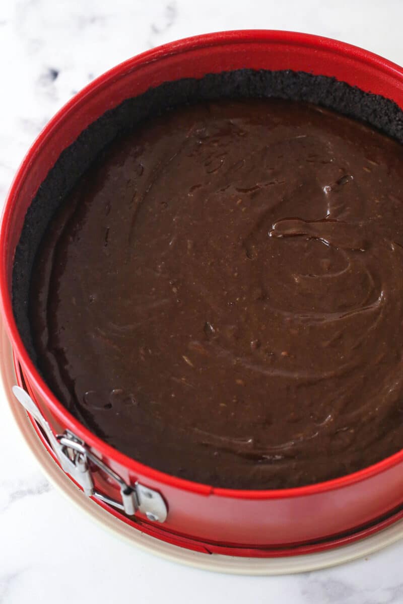 Brownie batter spread over an Oreo crust in a springform pan.