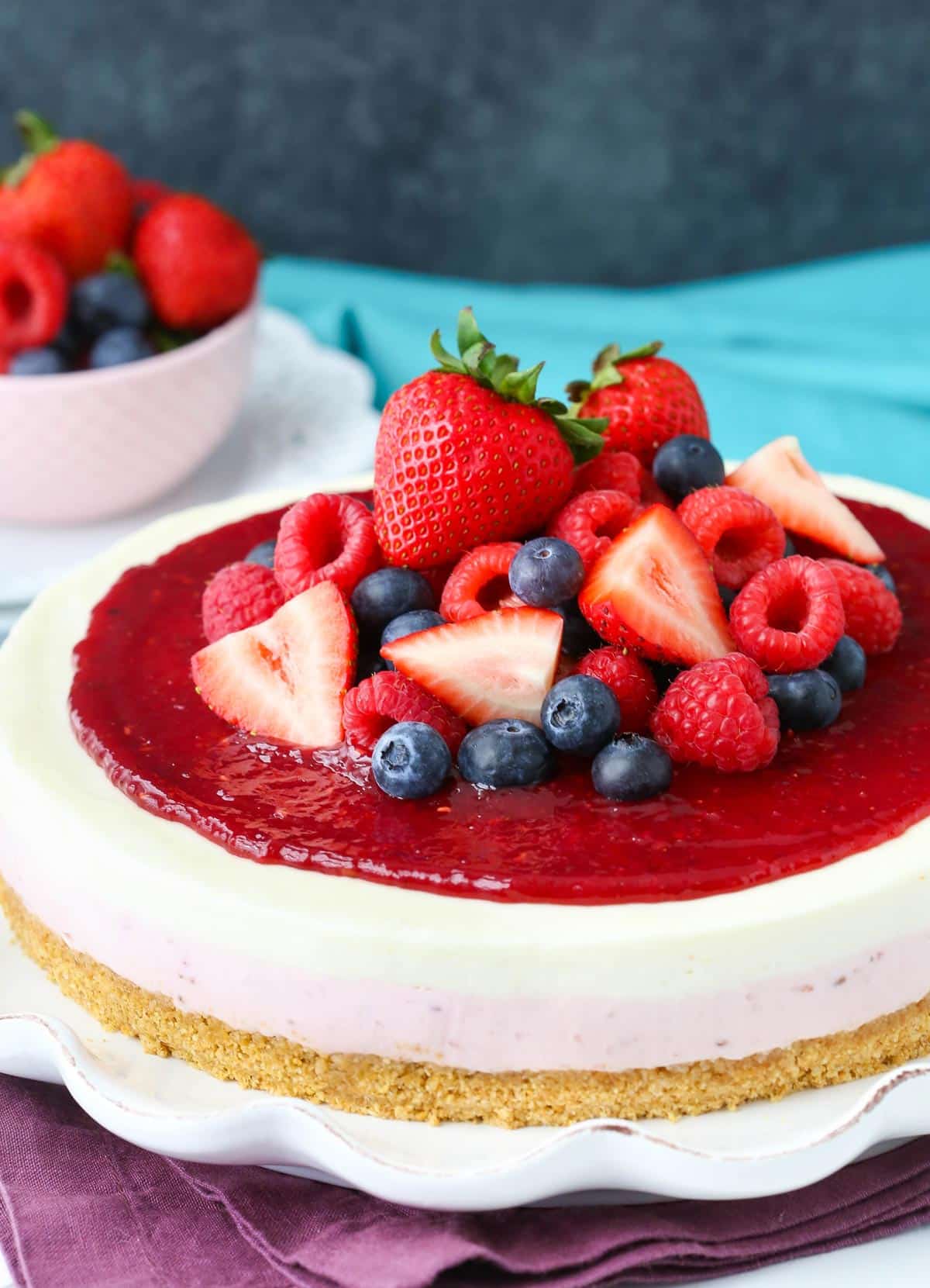 Close up of a no bake berry vanilla cheesecake on a white ruffled cake plate.