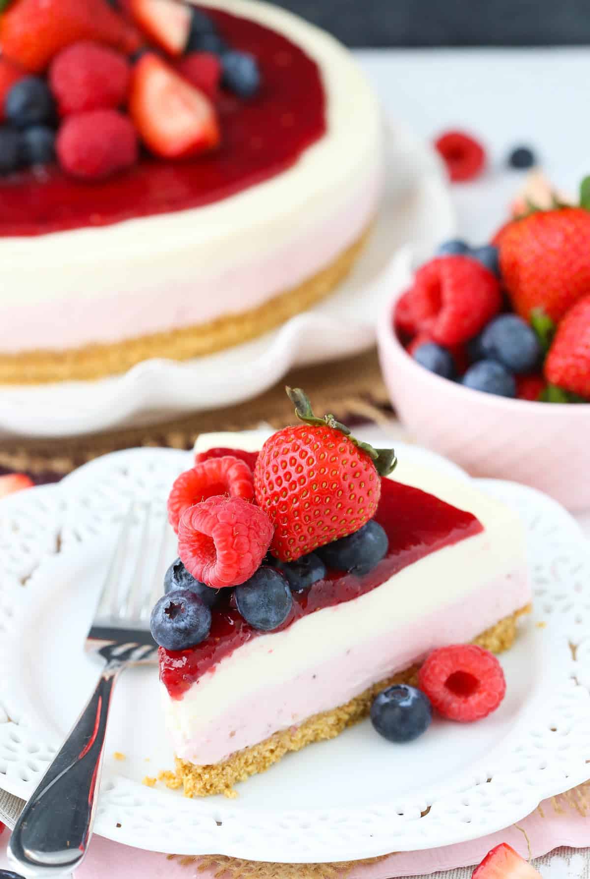 A slice of no bake berry vanilla cheesecake on a small white plate with the rest of the cheesecake in the background.