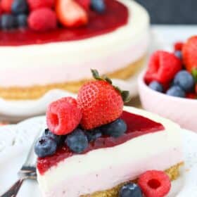 A slice of no bake berry vanilla cheesecake on a small white plate with the rest of the cake in the background.
