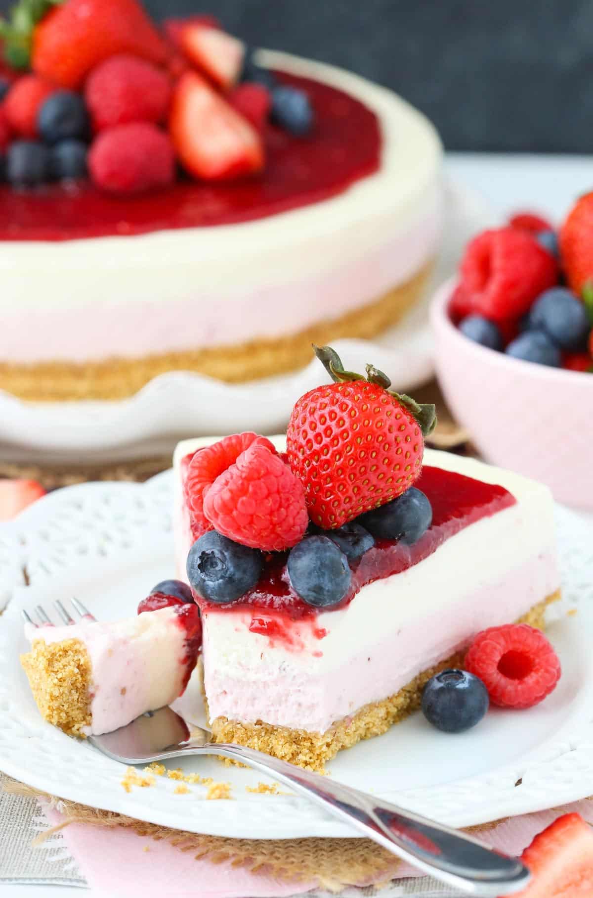 A slice of no bake berry vanilla cheesecake with a bite removed on a fork.