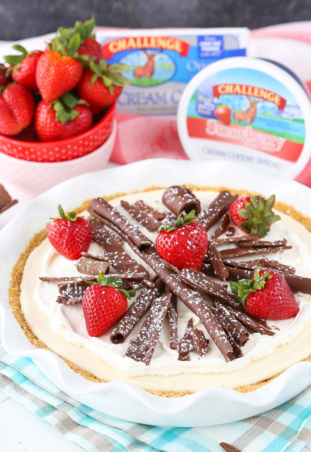 A no bake neapolitan cheesecake pie in a white pie pan with cream cheese in the background.