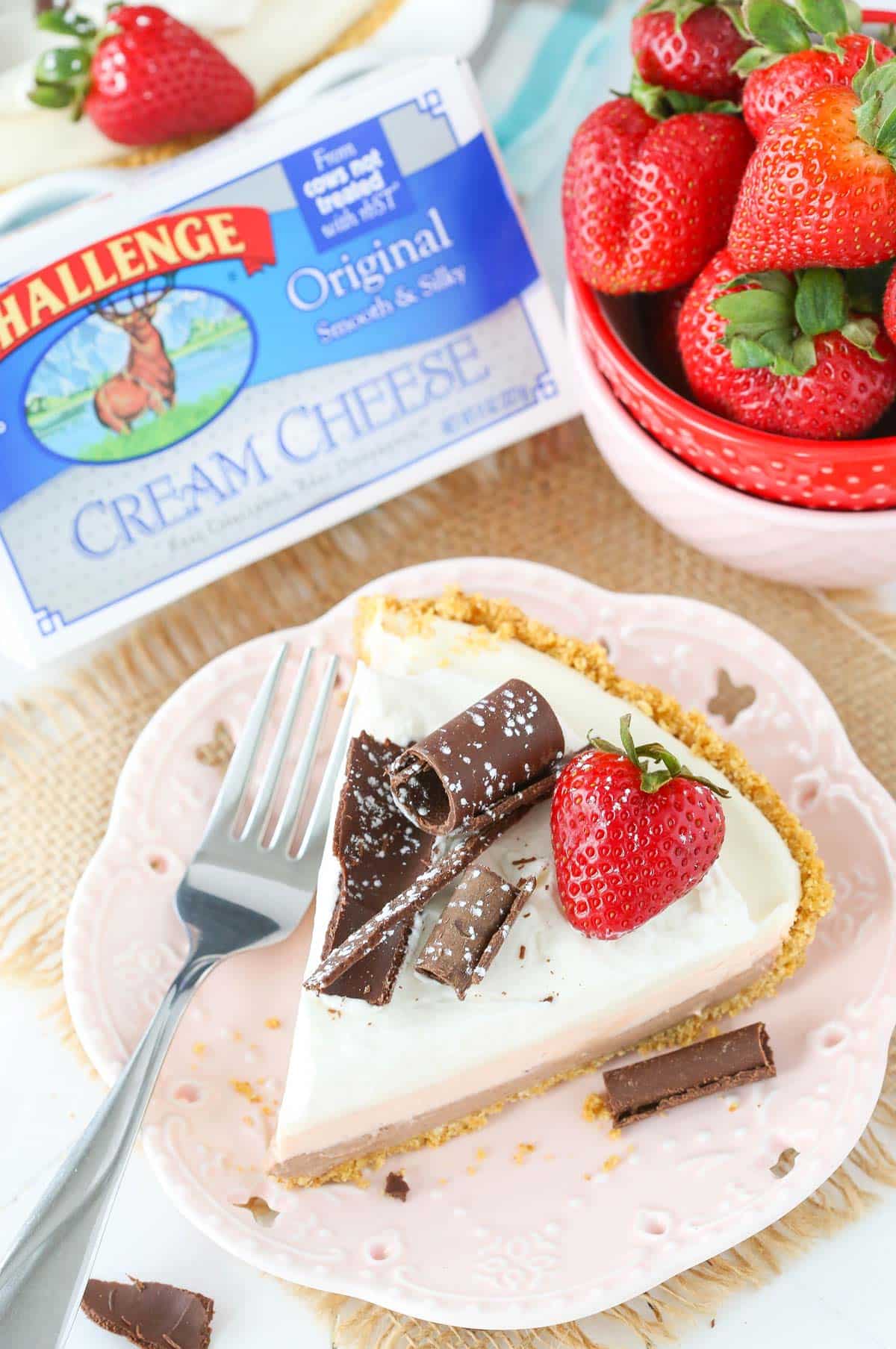 A slice of no bake neapolitan cheesecake pie on a small pink plate with a box of cream cheese in the background.