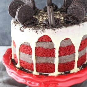 An Oreo cookie dough red velvet blondie layer cake on a red cake stand.