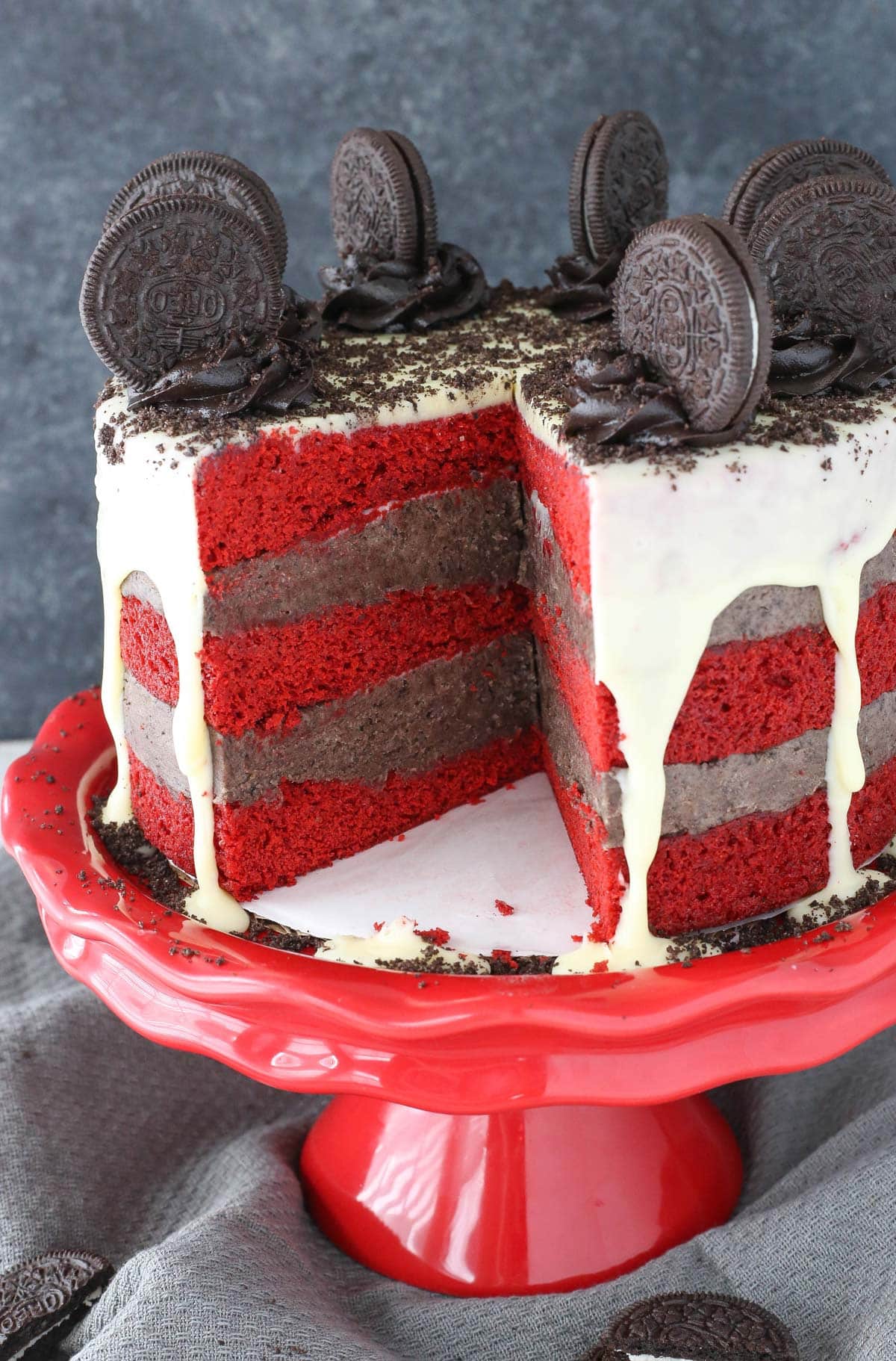An Oreo cookie dough red velvet blondie layer cake on a red cake stand with a slice removed to show layers.