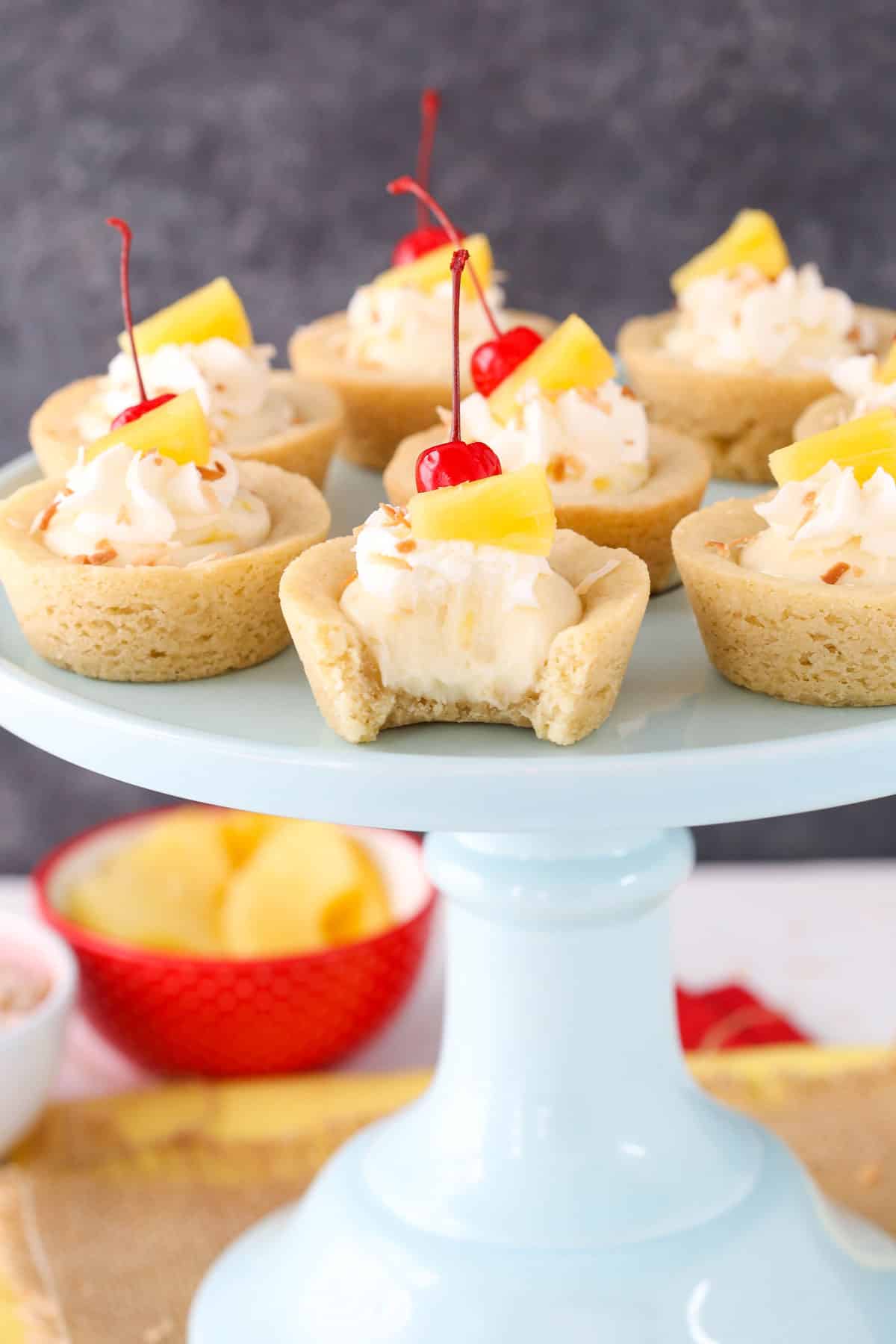 Pina colada cookie cups on a light blue cake stand with a bite removed from the front cookie.