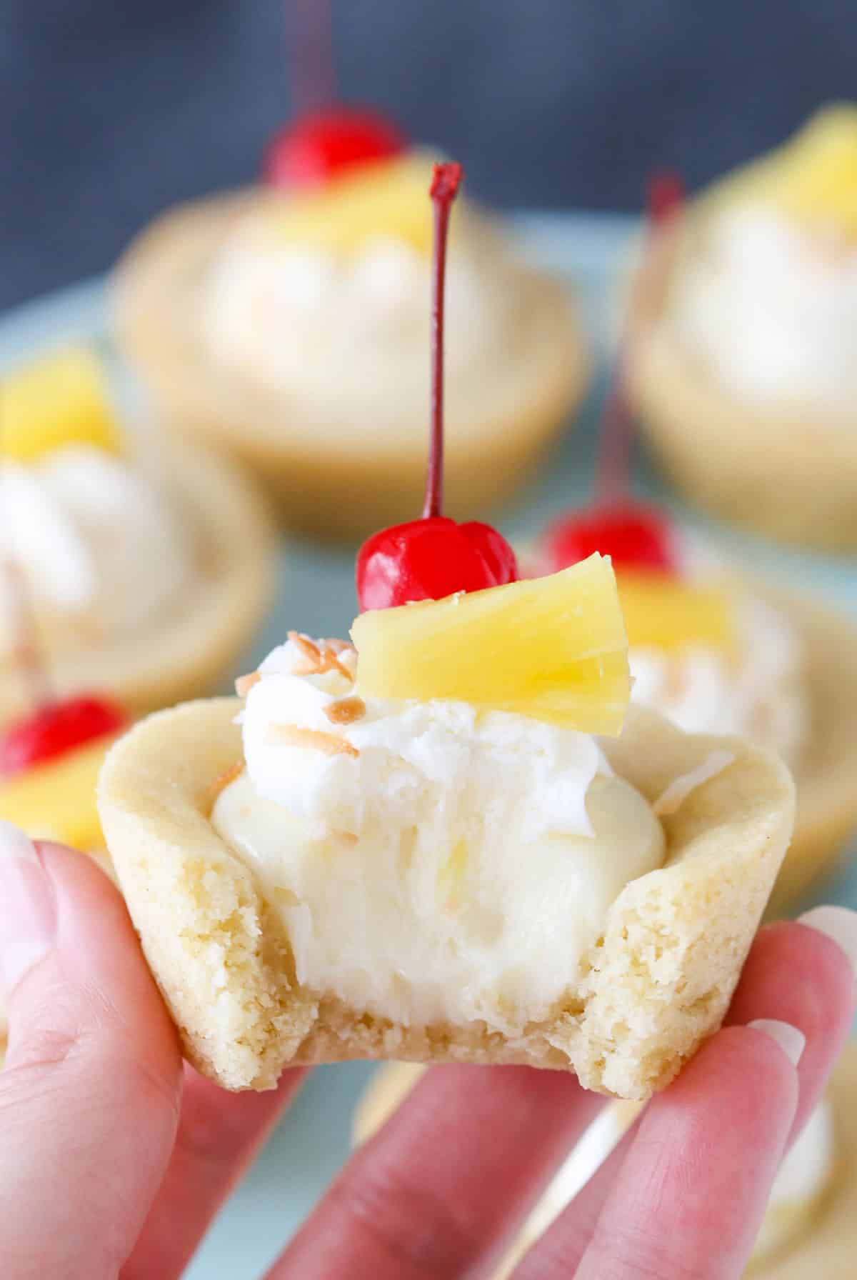 Hand holding a pina colada cookie cup with a bite taken out of it.