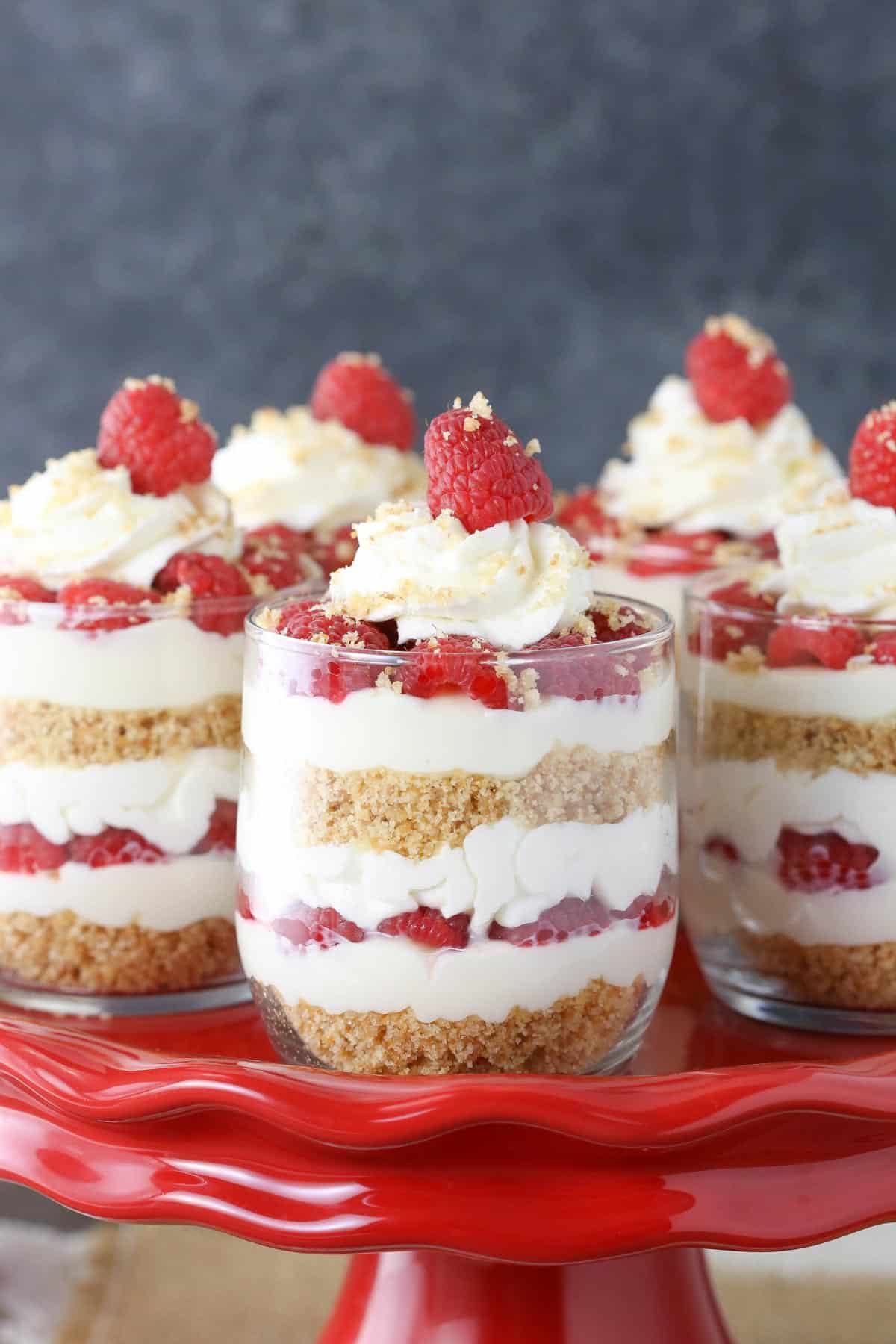 Side view of raspberry amaretto cheesecake trifles on a red cake stand.