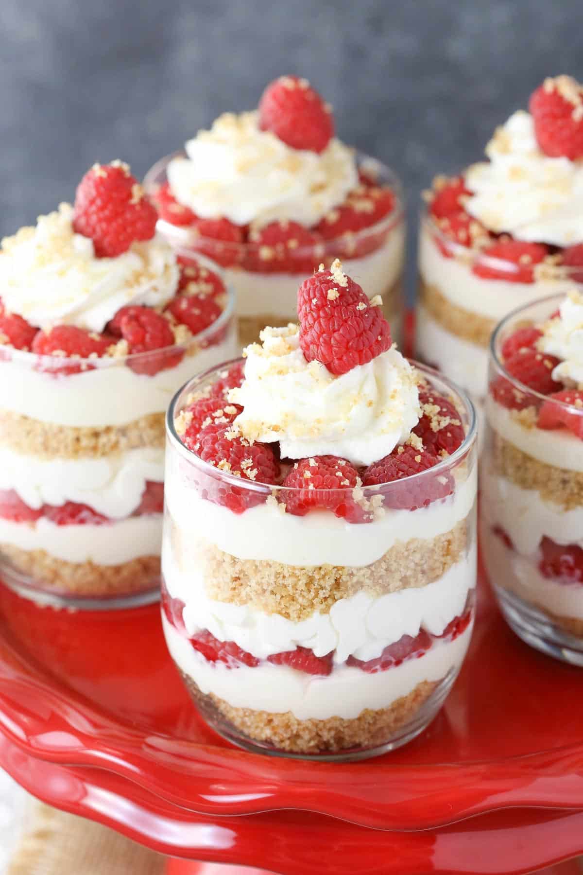 Five raspberry amaretto cheesecake trifles on a red plate.