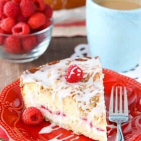 A slice of raspberry cream cheese coffee cake on a red plate next to a fork.