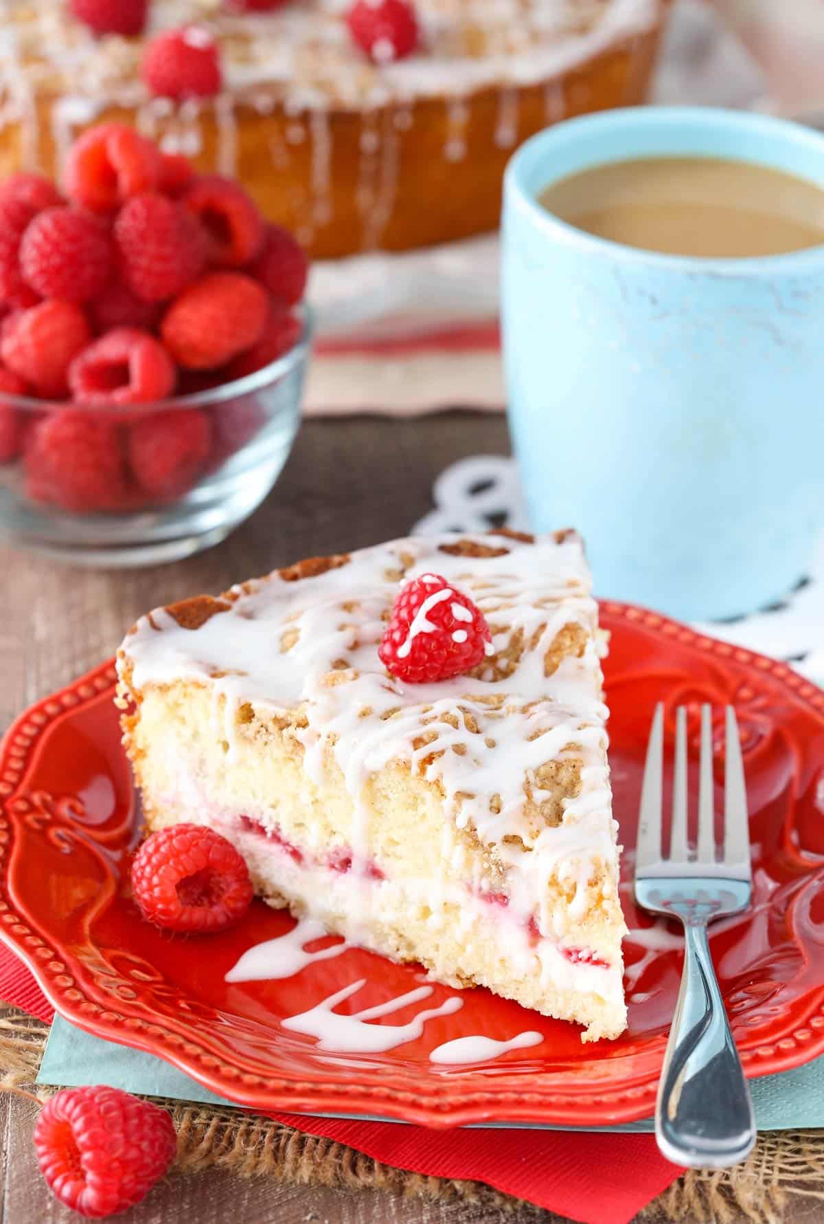 A slice of raspberry cream cheese coffee cake on a red plate next to a fork.
