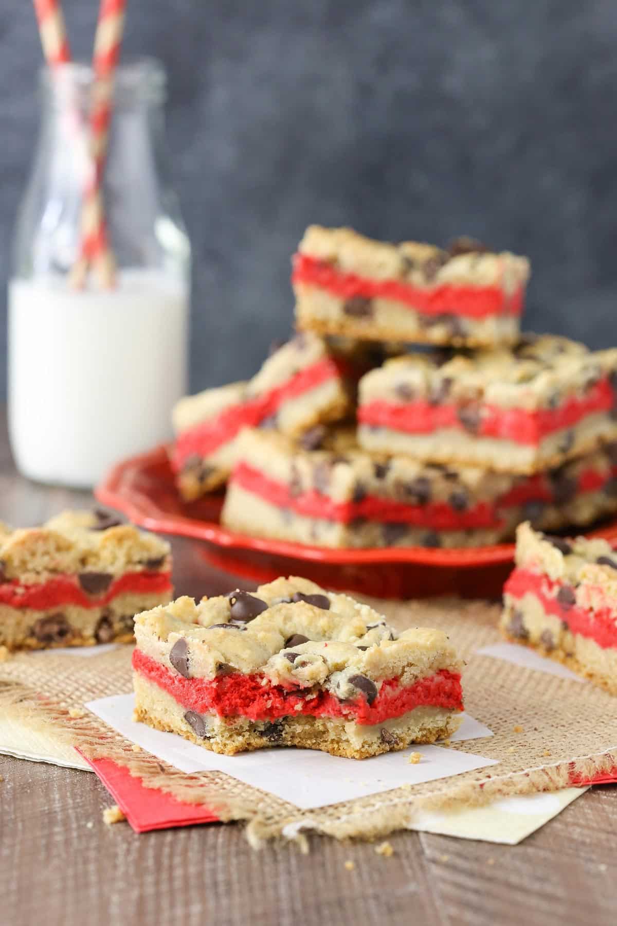 Close up of a red velvet cheesecake chocolate chip cookie bar with a bite out of it and more bars in the background.