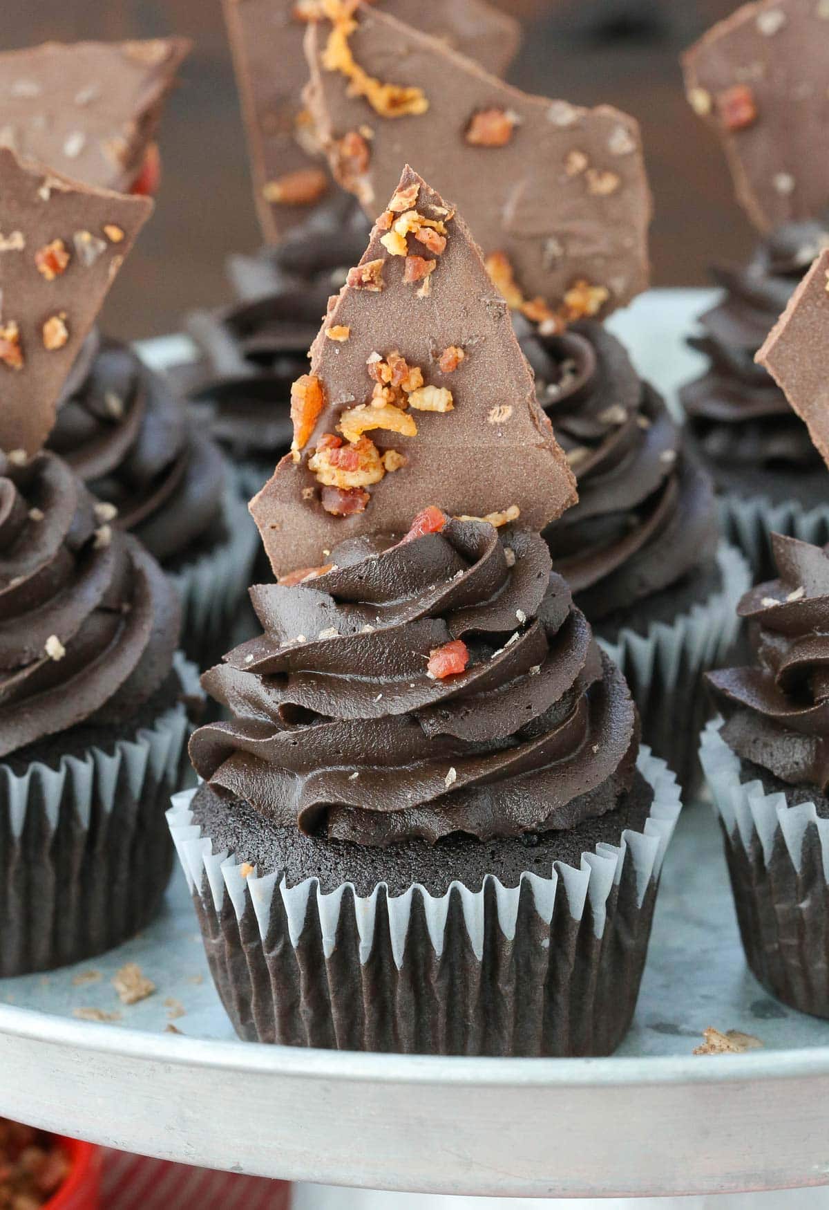 Close up of smokey bourbon chocolate cupcakes with bacon bark on a silver tray.