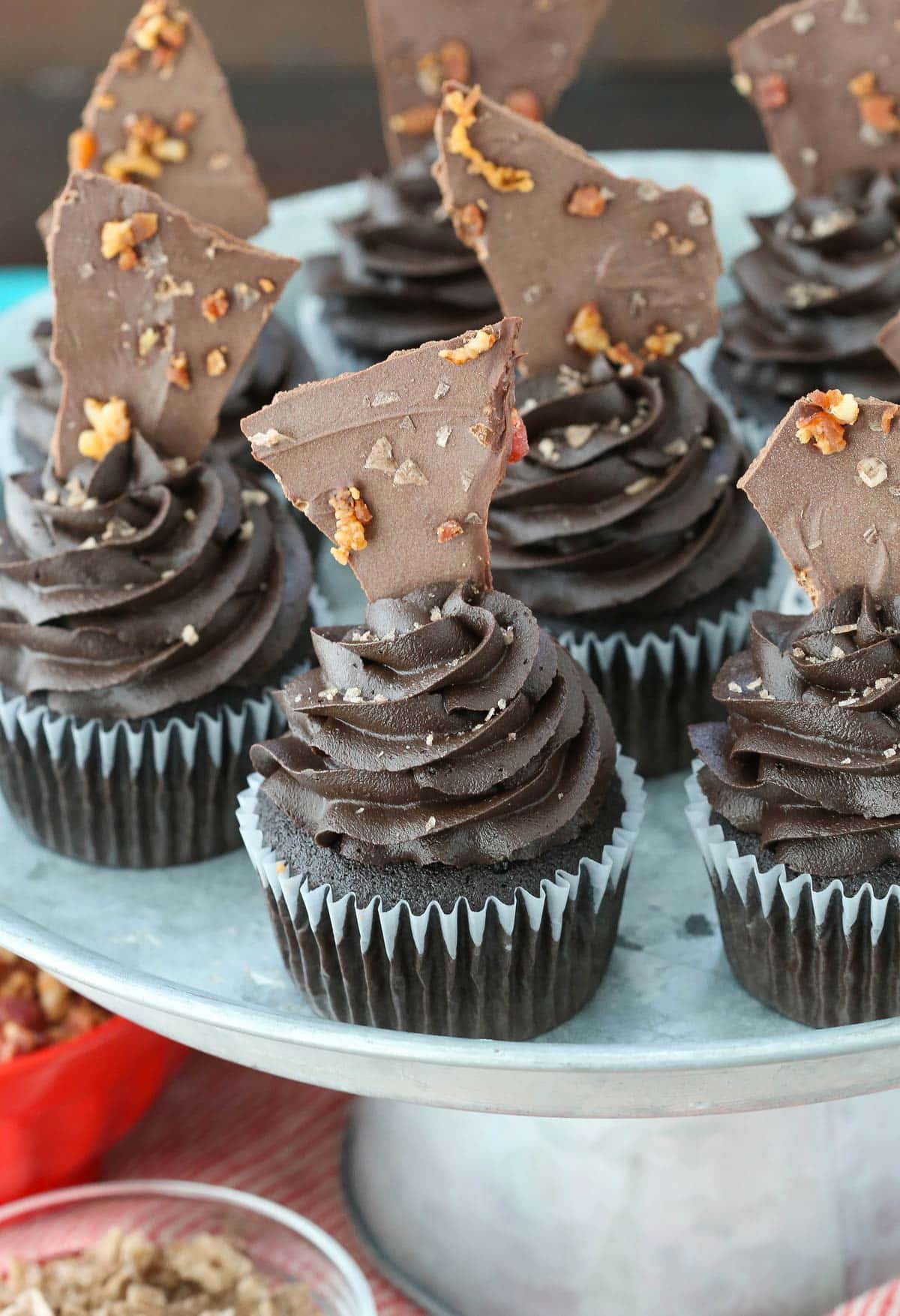 A silver cake stand covered with smokey bourbon chocolate cupcakes with bacon bark.