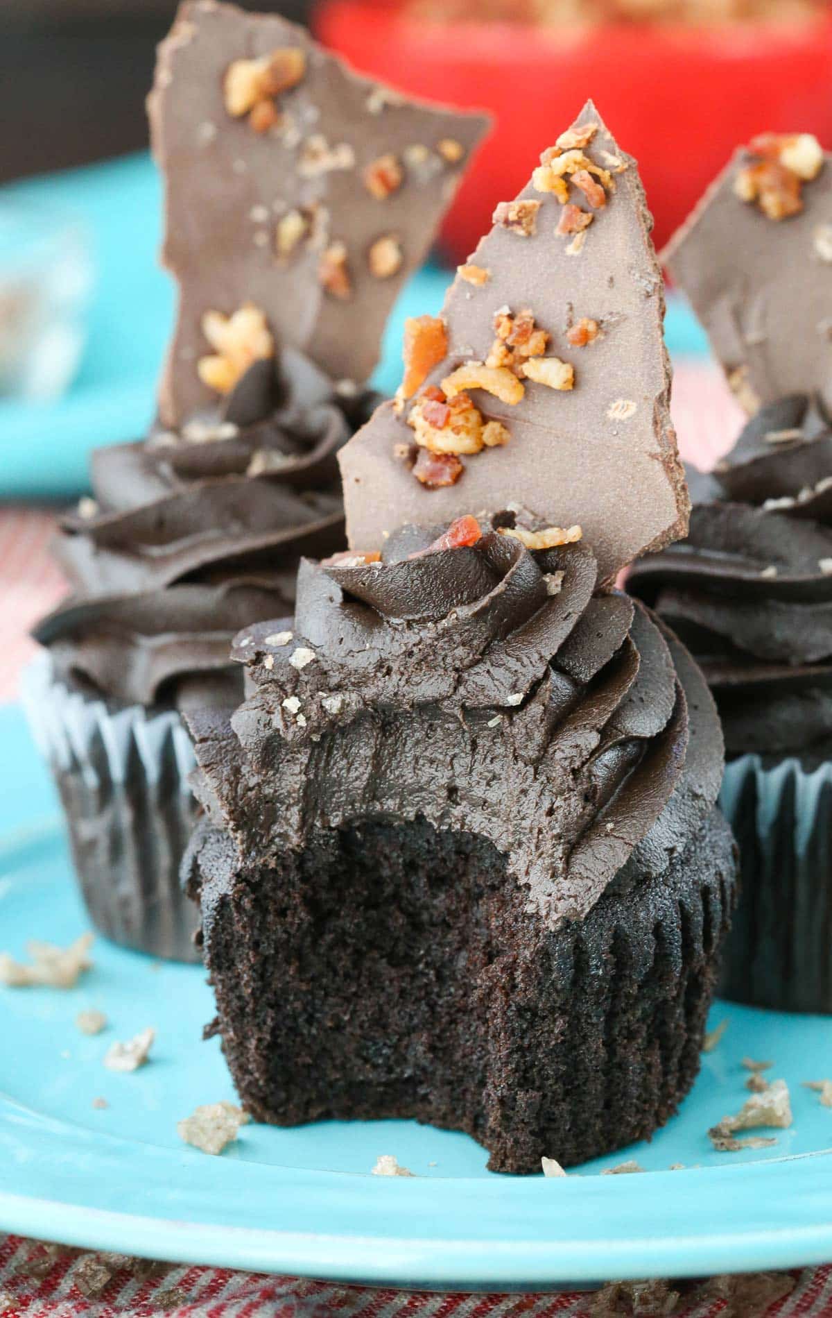Close up of a smokey bourbon chocolate cupcake with bacon bark on top and a bite removed.