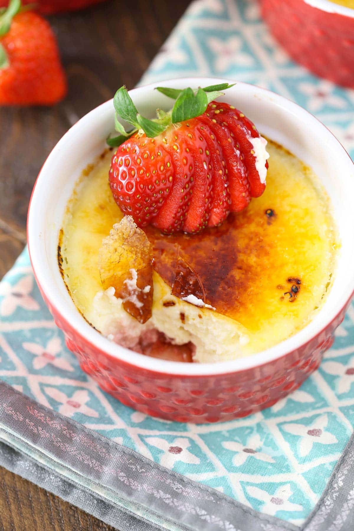 A red ramekin filled with strawberries brulee with a bite removed.