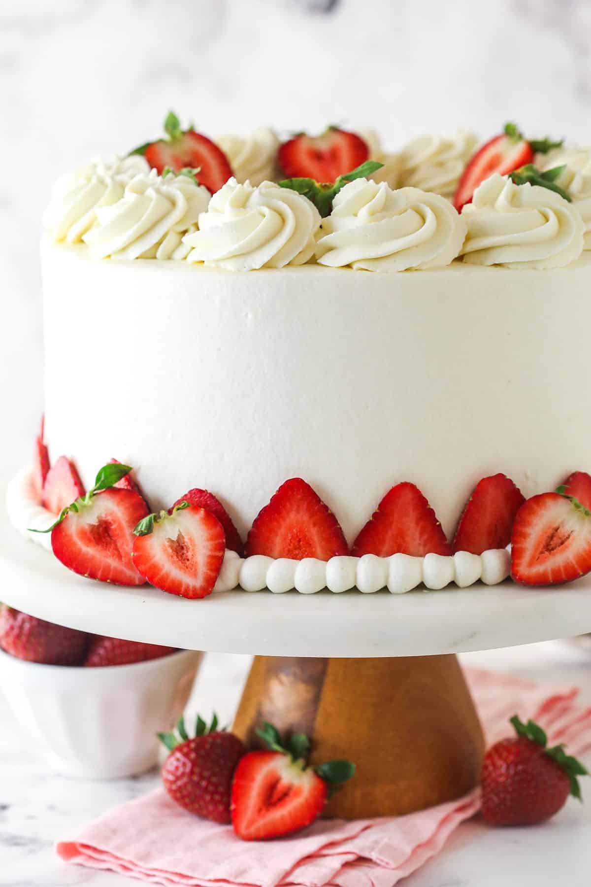 This strawberries and cream cheesecake cake layers strawberry cake, vanilla cheesecake, and cream cheese frosting for one incredible dessert. Strawberries and cream cheesecake cake on a cake stand.