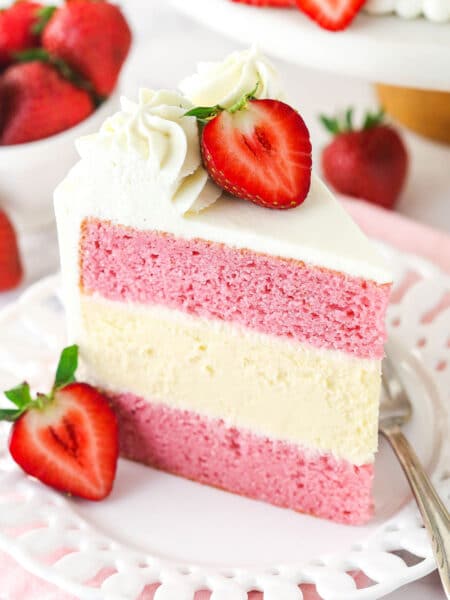 A slice of strawberries and cream cheesecake cake standing upright on a plate.