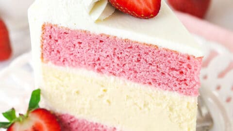 A slice of strawberries and cream cheesecake cake standing upright on a plate.