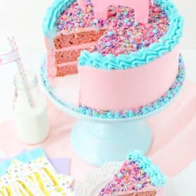 Top view of a strawberry layer cake with a slice removed on a small white plate.