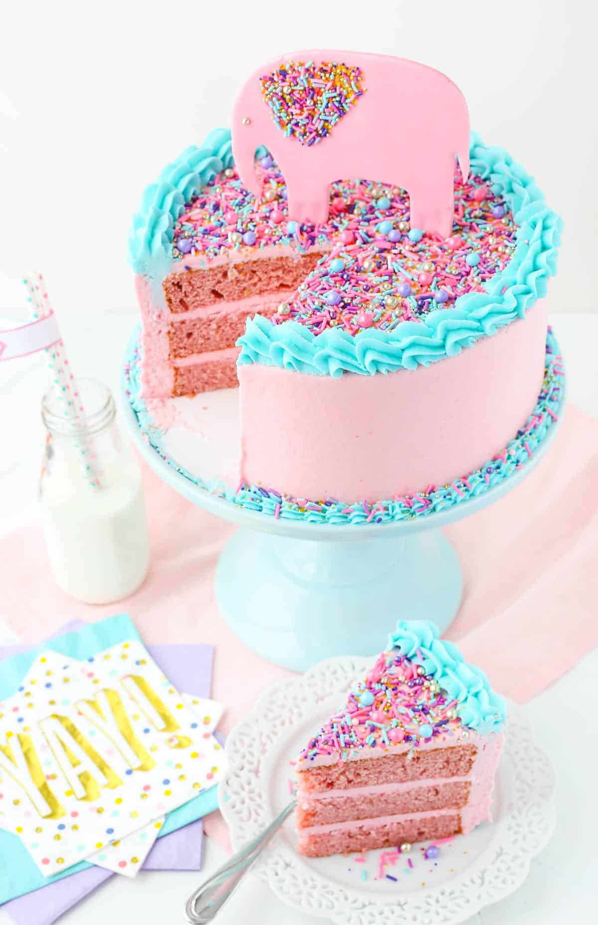 Top view of a strawberry layer cake with a slice removed on a small white plate.