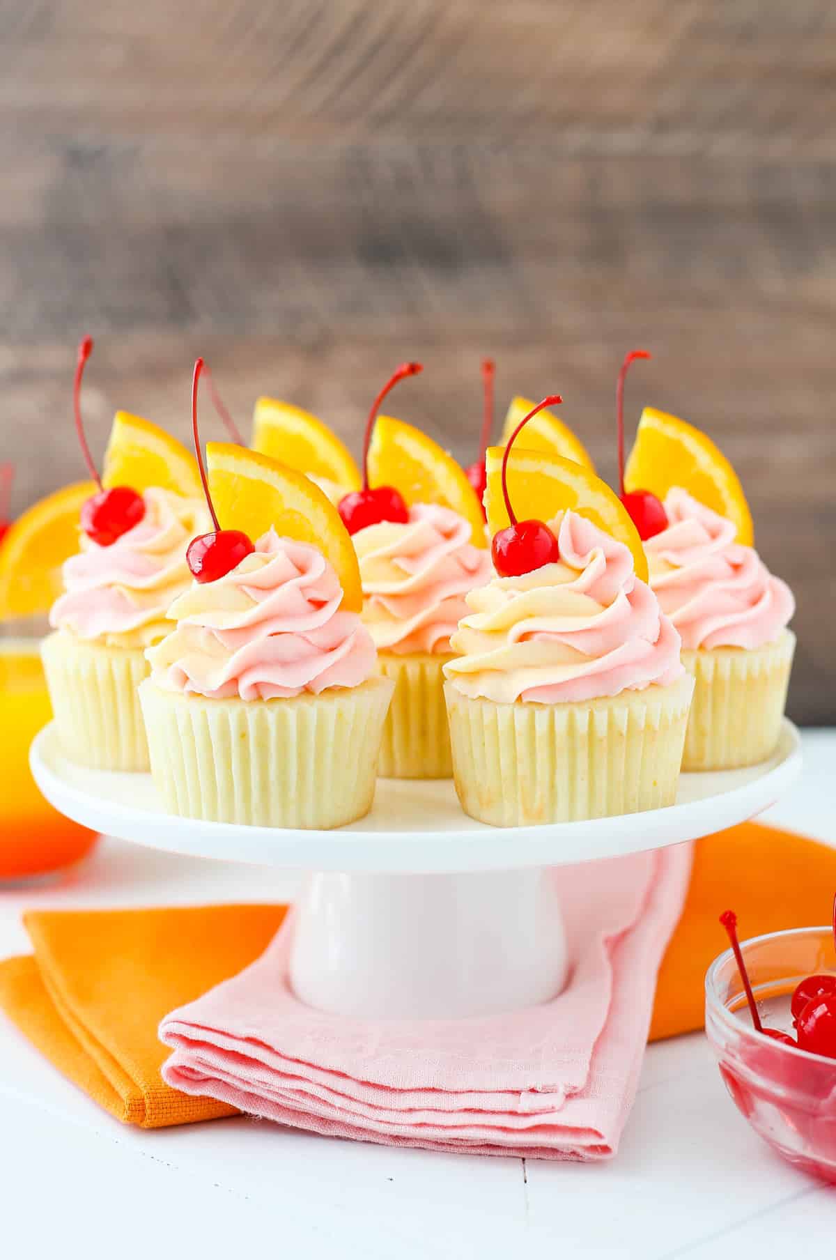 A white cake stand with several tequila sunrise cupcakes.