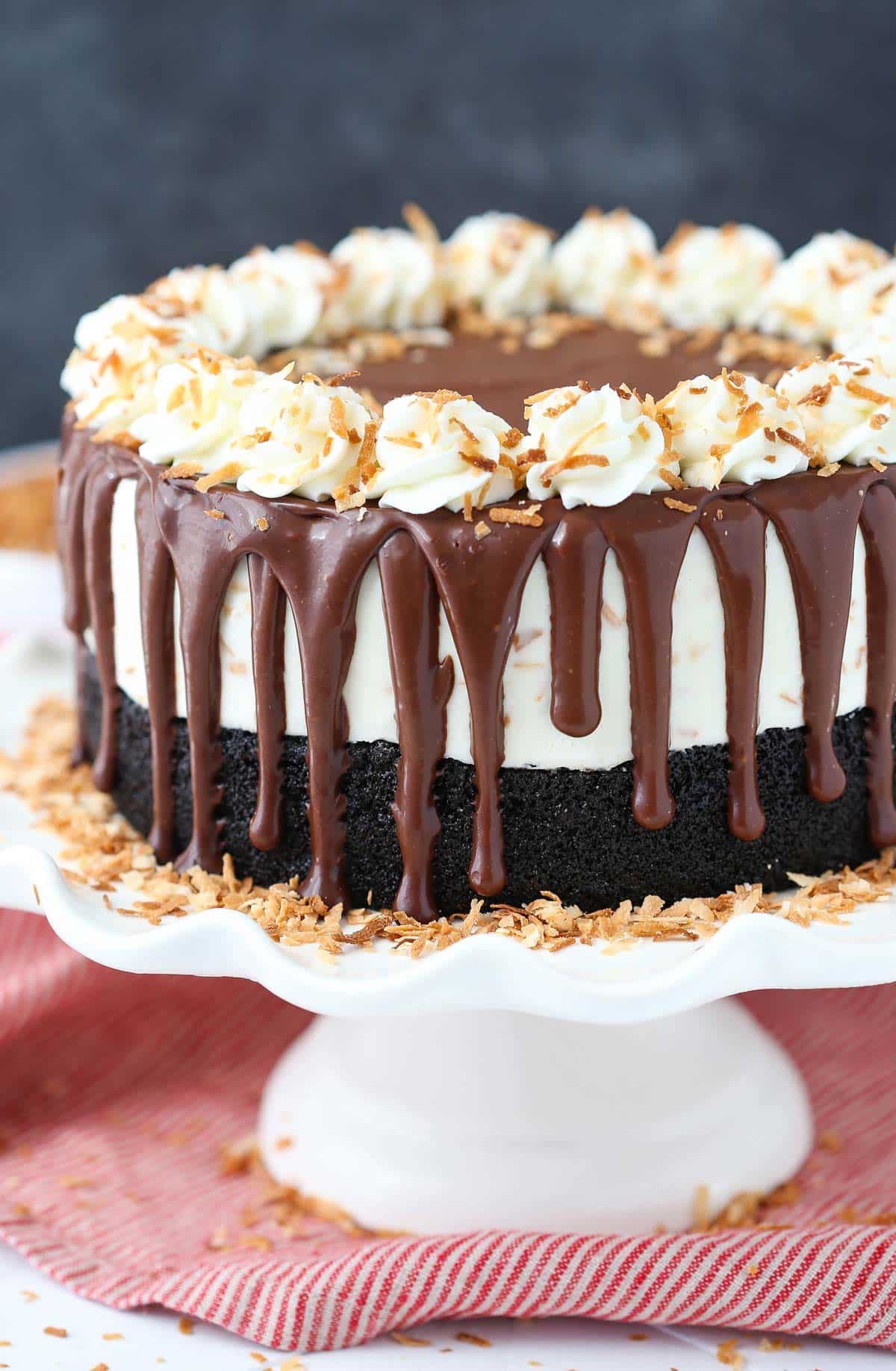 A toasted coconut chocolate ice cream cake on a white cake stand.