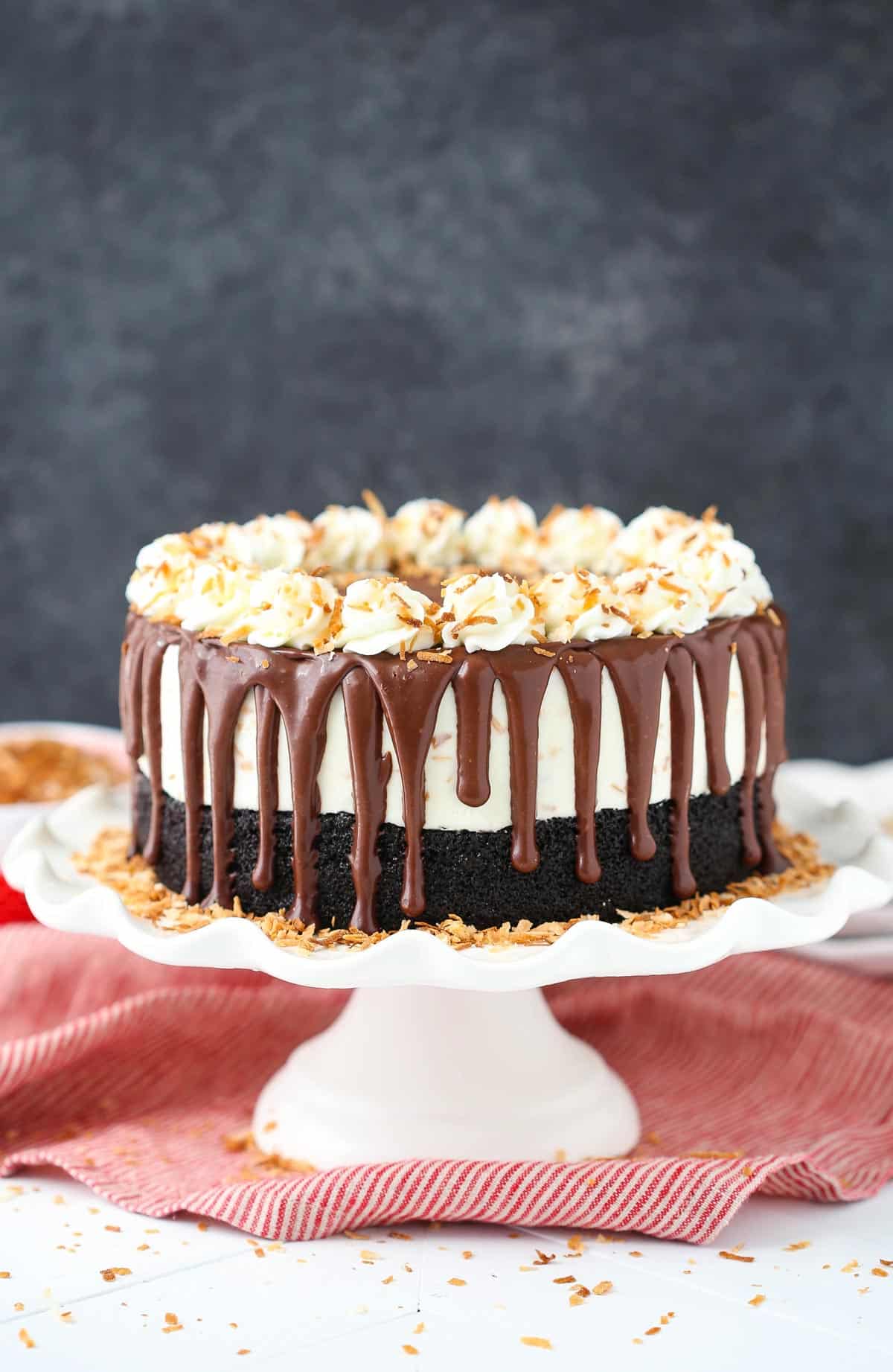 A toasted coconut chocolate ice cream cake on a white cake stand.