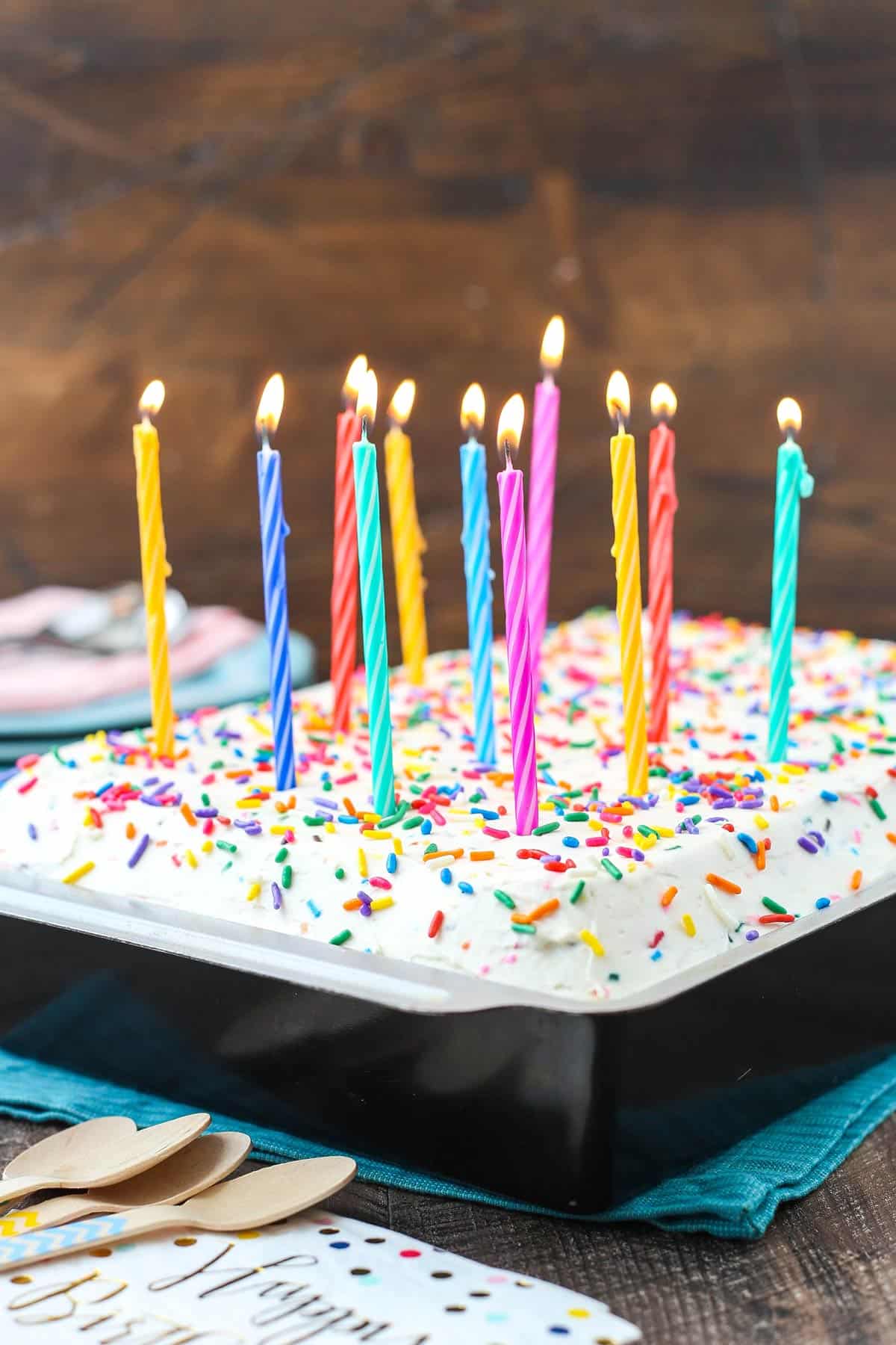 This epic birthday cake combines chewy chocolate chip cookies, creamy Funfetti cheesecake, moist cupcakes & fluffy cake batter whipped cream! A baking pan with an ultimate birthday cake topped with burning candles.