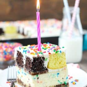 A slice of ultimate birthday cake with a burning candle on top.