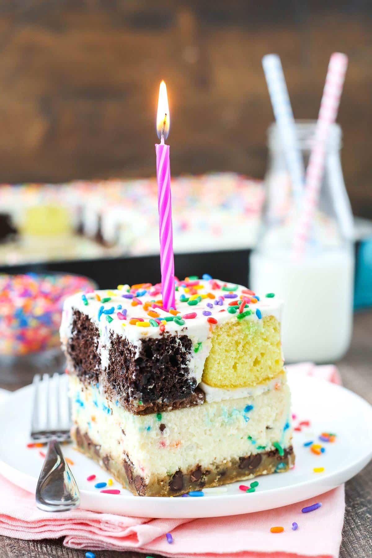 A slice of ultimate birthday cake with a burning candle on top.