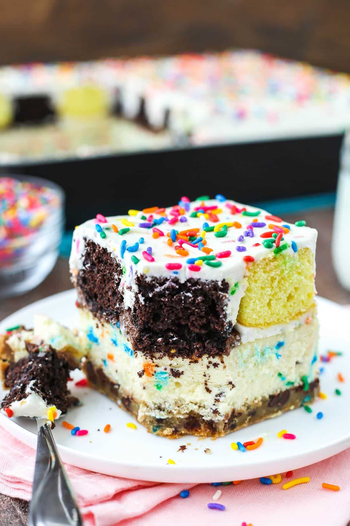 This epic birthday cake combines chewy chocolate chip cookies, creamy Funfetti cheesecake, moist cupcakes & fluffy cake batter whipped cream! A slice of ultimate birthday cake with a bite removed on a fork.