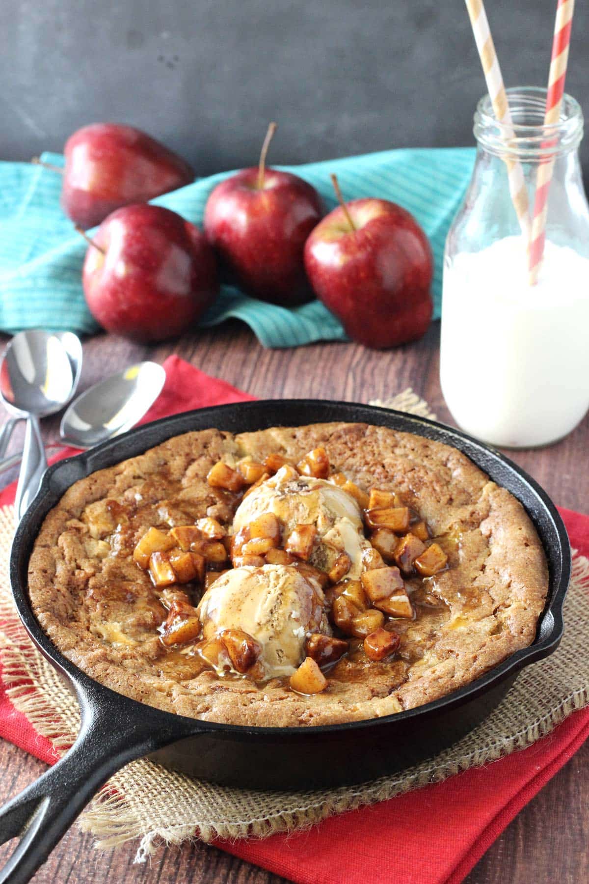 An apple cinnamon skillet blondie next to apples and milk.