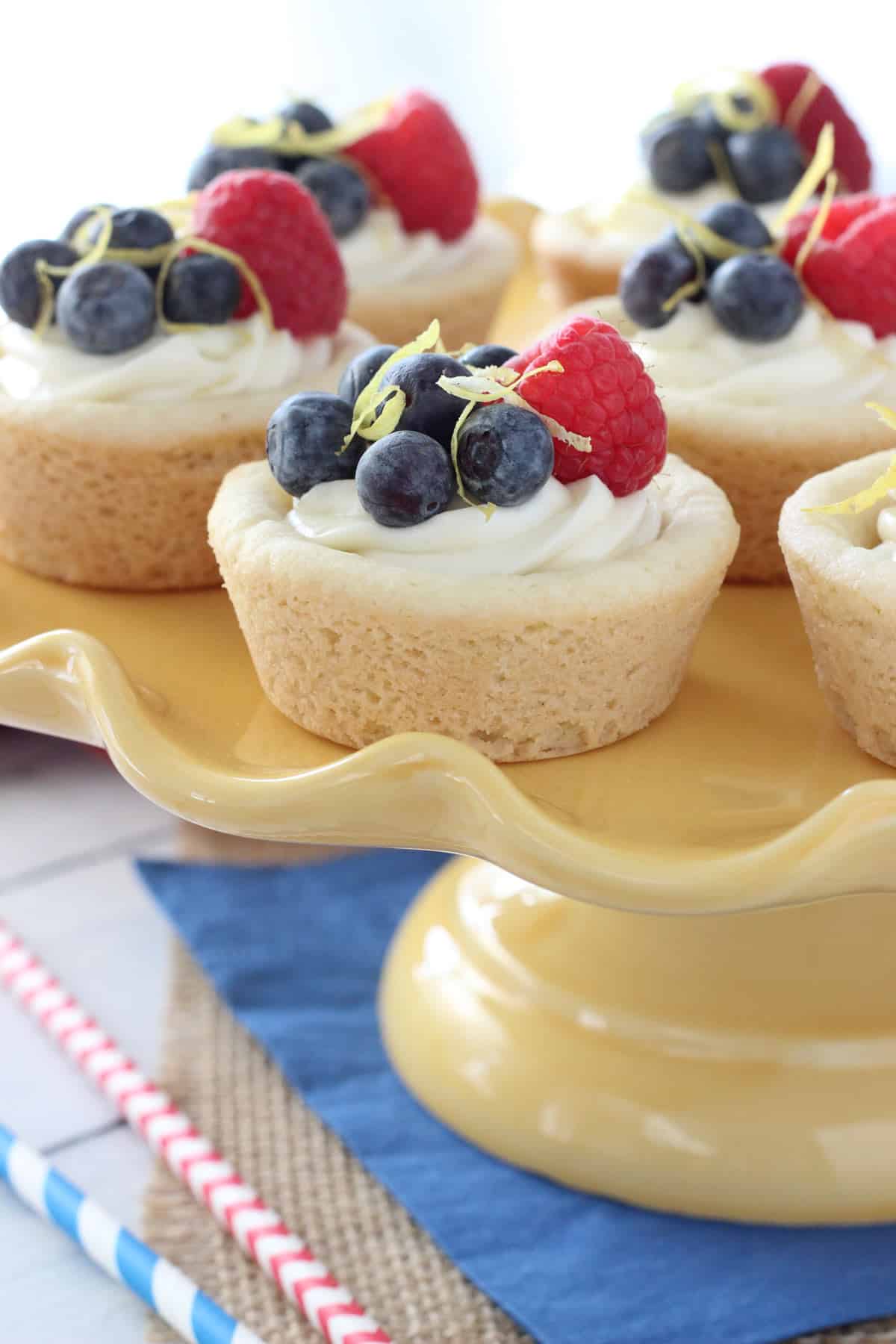 Close up of berry lemon cheesecake cookie cups on a yellow cake stand.