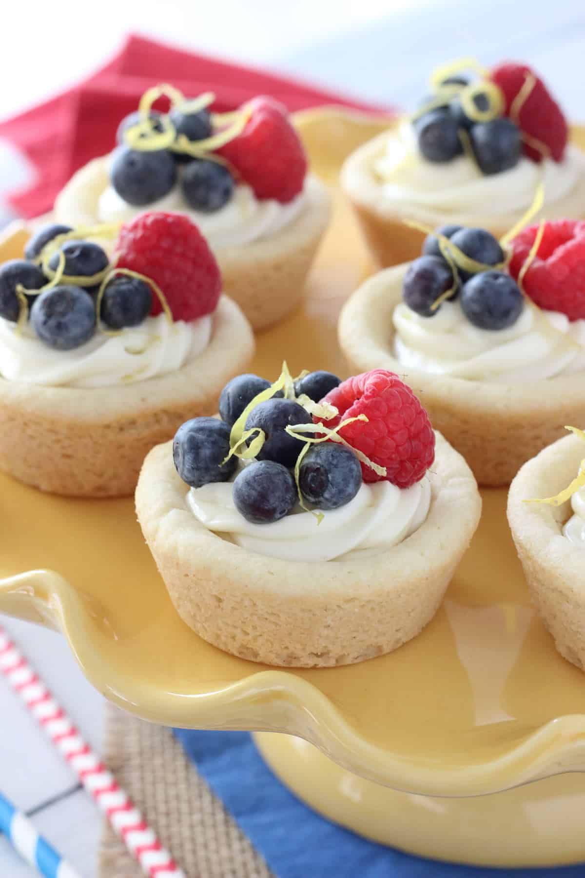 Close up of berry lemon cheesecake cookie cups on a yellow cake stand.