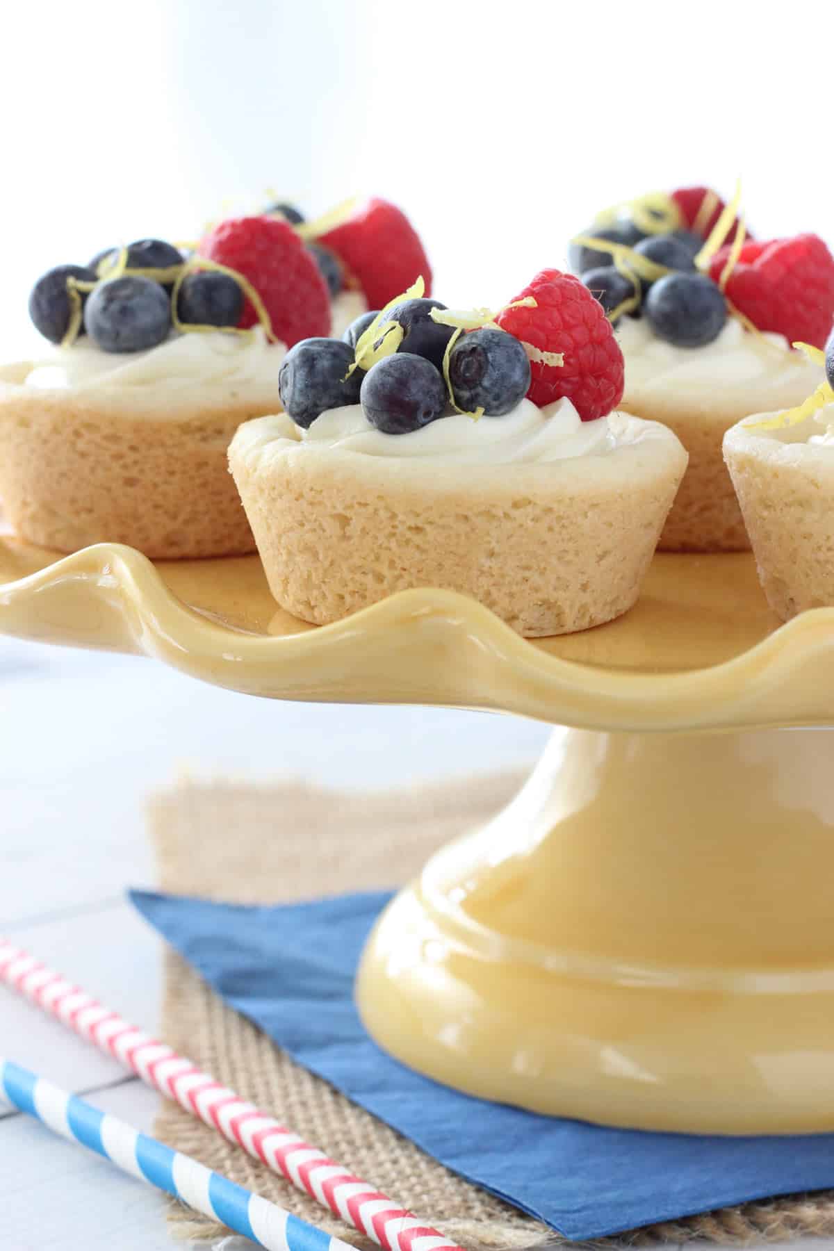 Side view of berry lemon cheesecake cookie cups on a yellow cake stand.