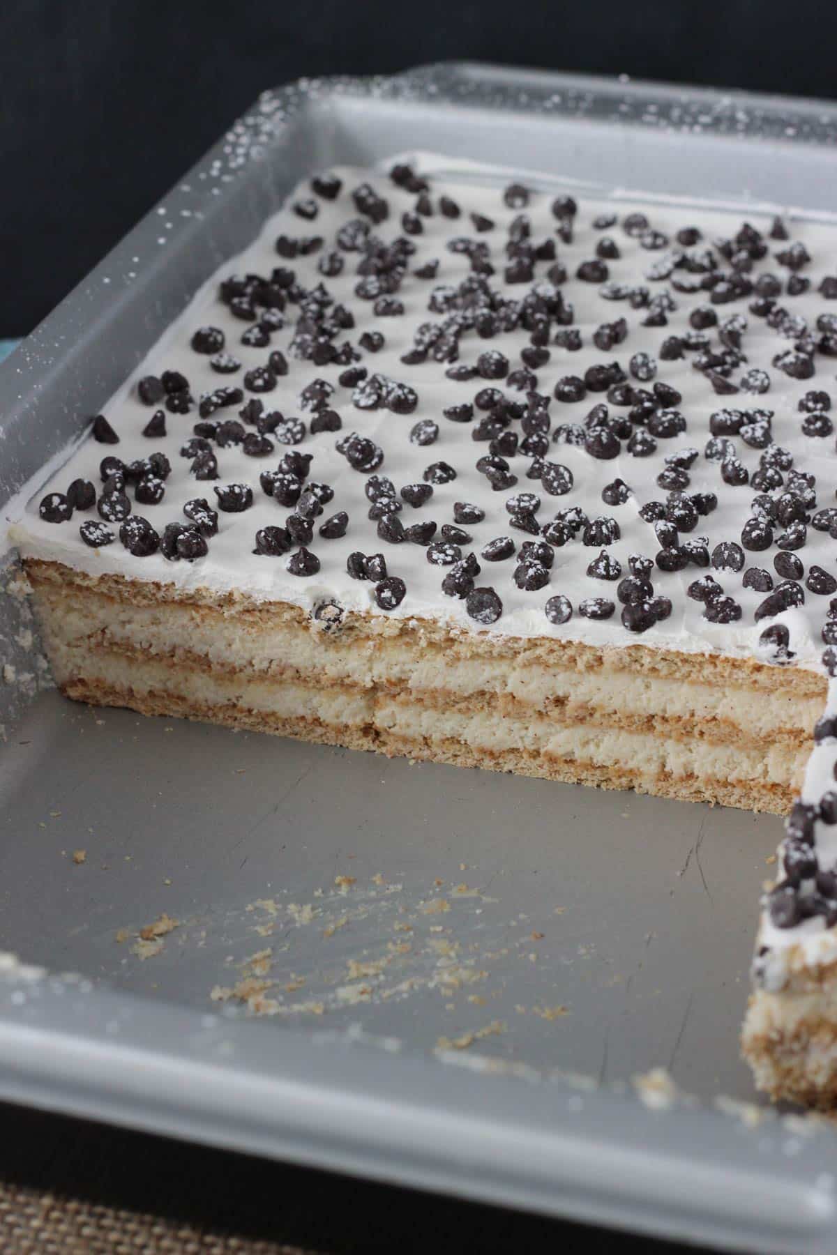 A cannoli icebox cake in a baking pan with a few slices removed.