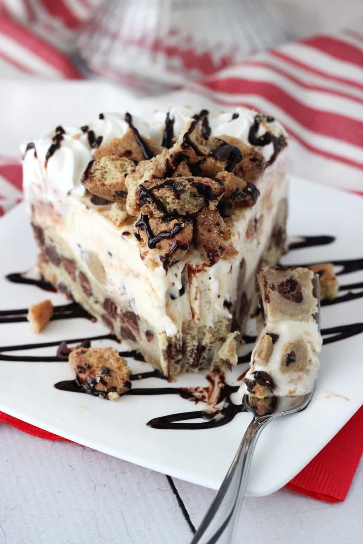 A slice of chocolate chip cookie ice cream cake on a white plate with a bite removed on a fork.