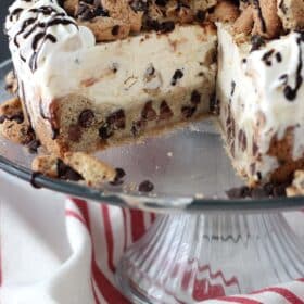 A chocolate chip cookie ice cream cake on a cake plate with a slice removed to show layers.