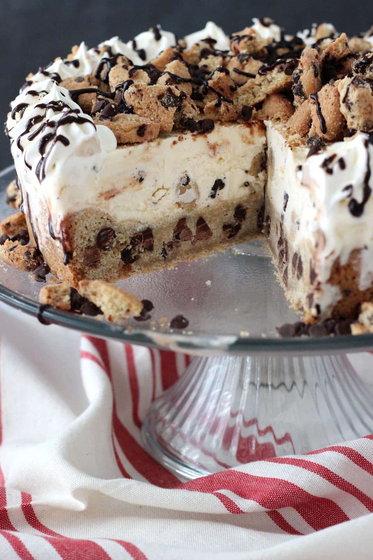 A chocolate chip cookie ice cream cake on a cake plate with a slice removed to show layers.