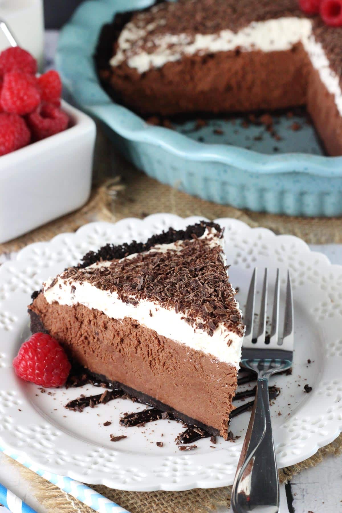 A slice of chocolate truffle pie on a white plate with the rest of the pie in the background.