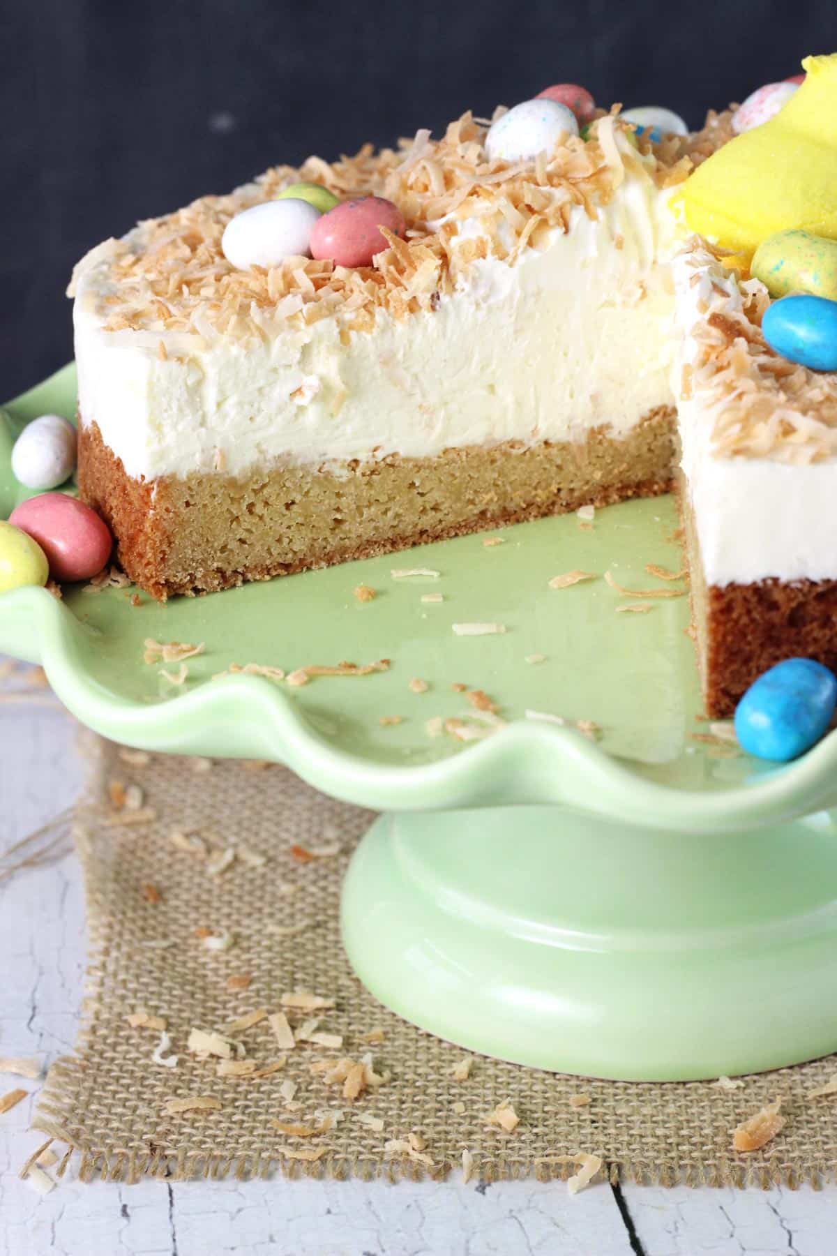 A coconut blondie cheesecake on a green ruffled cake plate with a slice removed to show layers.