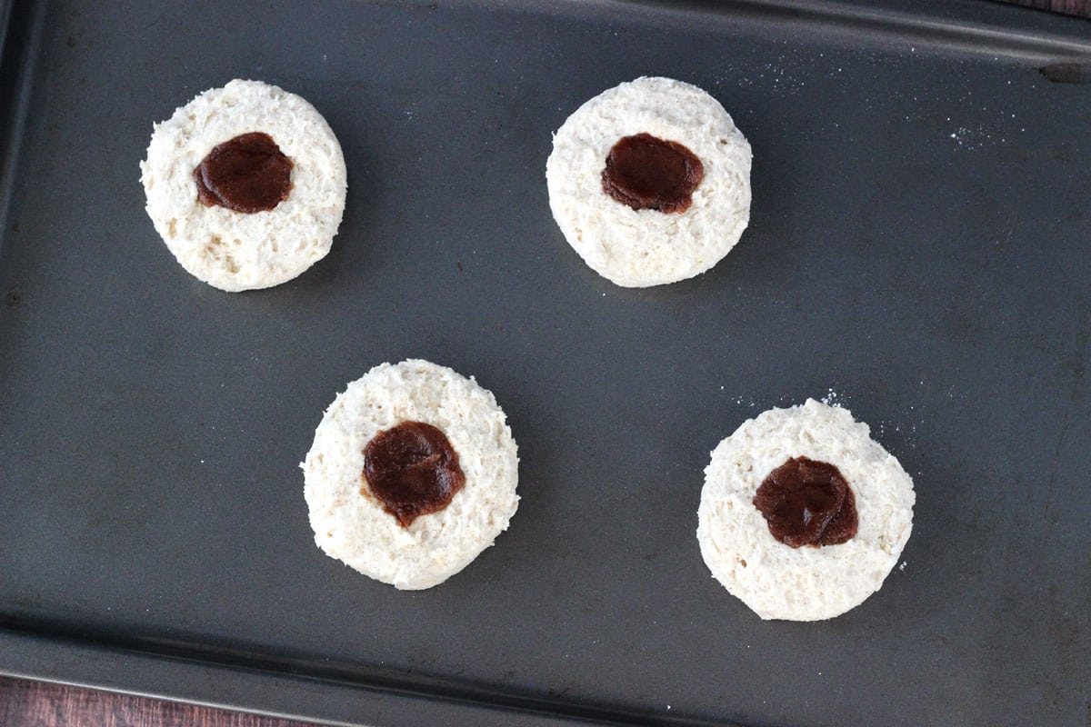 Four biscuits with cinnamon on top on a baking sheet.