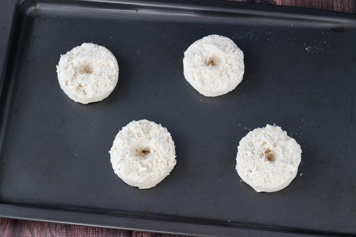 Four dough biscuits with holes pressed into the center on a baking tray.